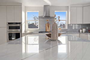 Kitchen with double oven, decorative backsplash, a wealth of natural light, and wall chimney exhaust hood