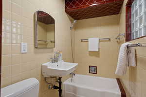 Full bathroom with tiled shower / bath, toilet, tile walls, and sink