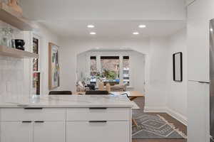 Kitchen with light stone countertops, kitchen peninsula, dark hardwood / wood-style floors, and white cabinetry