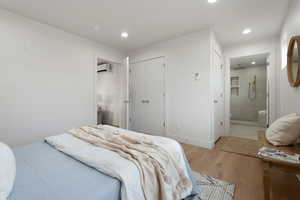 Bedroom with light hardwood / wood-style floors, an AC wall unit, connected bathroom, and a closet