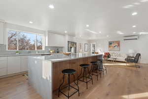 Kitchen featuring white cabinets, light hardwood / wood-style flooring, a wall mounted AC, and a spacious island