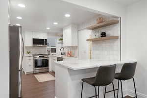 Kitchen featuring kitchen peninsula, appliances with stainless steel finishes, tasteful backsplash, dark wood-type flooring, and white cabinetry