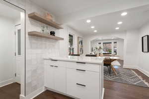 Kitchen with light stone counters, white cabinetry, kitchen peninsula, and dark wood-type flooring