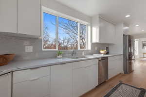 Kitchen with white cabinets, sink, light hardwood / wood-style floors, light stone counters, and stainless steel appliances