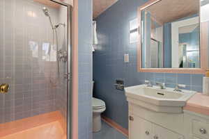 Bathroom featuring backsplash, vanity, tile walls, toilet, and a shower with shower door