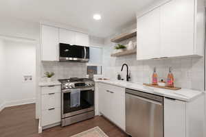 Kitchen with decorative backsplash, white cabinetry, dark wood-type flooring, and stainless steel appliances