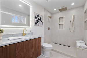 Bathroom with a tile shower, vanity, and toilet