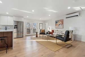 Living room with a wall mounted air conditioner, light wood-type flooring, and french doors