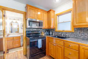 Kitchen featuring backsplash, light hardwood / wood-style flooring, black electric range oven, and sink