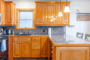 Kitchen with a breakfast bar, backsplash, black range, sink, and decorative light fixtures