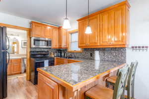 Kitchen with black appliances, a kitchen breakfast bar, hanging light fixtures, light hardwood / wood-style flooring, and kitchen peninsula