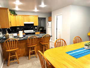 Kitchen featuring electric range, decorative backsplash, a textured ceiling, light colored carpet, and kitchen peninsula