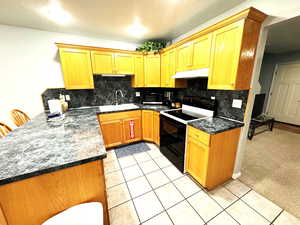 Kitchen featuring sink, decorative backsplash, white range with electric cooktop, dark stone counters, and light carpet