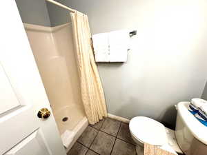 Bathroom with tile patterned flooring, toilet, and curtained shower