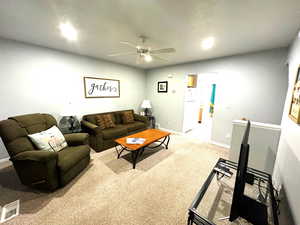 Living room with ceiling fan, carpet floors, and a textured ceiling