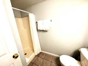 Bathroom with tile patterned flooring, a shower with curtain, a textured ceiling, and toilet