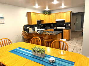 Kitchen with white range with electric cooktop, sink, light tile patterned floors, tasteful backsplash, and kitchen peninsula