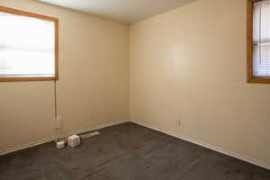 Unfurnished room featuring dark colored carpet and plenty of natural light