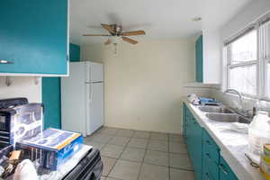 Kitchen with ceiling fan, sink, tile counters, white refrigerator, and light tile patterned flooring