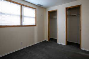 Unfurnished bedroom with dark colored carpet and two closets