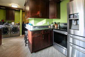 Kitchen featuring appliances with stainless steel finishes, light wood-type flooring, independent washer and dryer, and dark stone counters