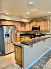 Kitchen featuring a breakfast bar area, kitchen peninsula, stainless steel appliances, and a textured ceiling