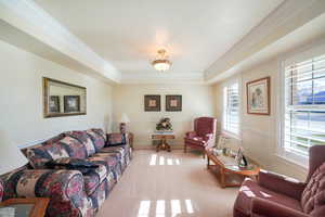 Living room with a tray ceiling, crown molding, and light colored carpet