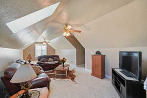 Living room with vaulted ceiling with skylight, ceiling fan, light carpet, and a textured ceiling