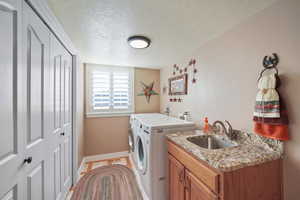 Clothes washing area featuring a textured ceiling, cabinets, sink, and washing machine and clothes dryer