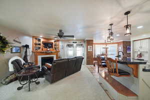 Carpeted living room with a textured ceiling, a tile fireplace, and ceiling fan with notable chandelier