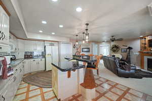 Kitchen featuring pendant lighting, a center island, ceiling fan, white fridge with ice dispenser, and a breakfast bar area