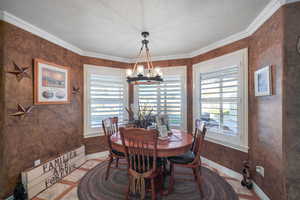 Tiled dining area with plenty of natural light, ornamental molding, a textured ceiling, and an inviting chandelier