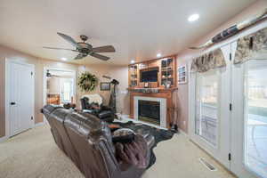 Carpeted living room featuring ceiling fan and a tile fireplace