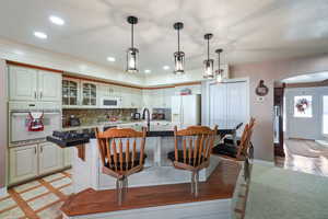 Kitchen featuring backsplash, white appliances, decorative light fixtures, a center island with sink, and a breakfast bar area