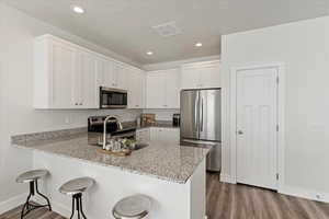 Kitchen with white cabinets, a kitchen bar, kitchen peninsula, and appliances with stainless steel finishes