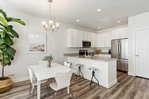 Kitchen featuring white cabinetry, hanging light fixtures, stainless steel appliances, light stone counters, and kitchen peninsula