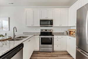 Kitchen featuring white cabinetry, sink, dark wood-type flooring, stainless steel appliances, and light stone counters