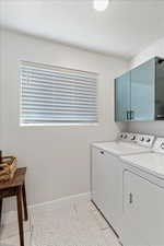 Clothes washing area with cabinets, independent washer and dryer, and light tile patterned flooring