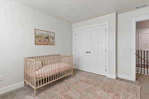 Bedroom featuring a closet, light colored carpet, and a nursery area