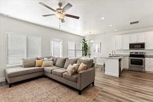 Living room with sink, ceiling fan with notable chandelier, and light wood-type flooring