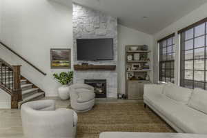 Living room with a stone fireplace, lofted ceiling, and light hardwood / wood-style flooring