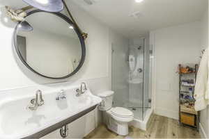 Bathroom featuring hardwood / wood-style flooring, toilet, a shower with door, and sink