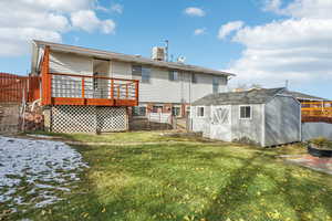 Back of property featuring a lawn, central AC unit, a shed, and a deck