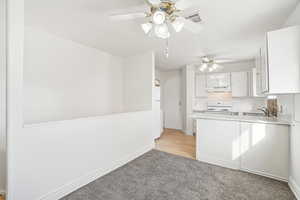 Kitchen featuring ceiling fan, sink, white range with electric stovetop, kitchen peninsula, and white cabinets