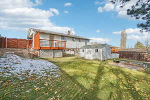 Rear view of property featuring a storage unit, cooling unit, a yard, and a wooden deck