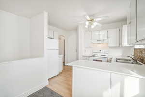 Kitchen featuring kitchen peninsula, white appliances, sink, light hardwood / wood-style floors, and white cabinetry