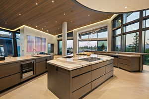 Kitchen with a spacious island, modern cabinets, high vaulted ceiling, floor to ceiling windows, and wine cooler