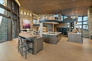 Kitchen with a large island with sink, a towering ceiling, light countertops, light wood-style flooring, and wooden ceiling