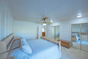 Bedroom with ceiling fan, light colored carpet, and two closets