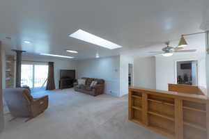 Living room featuring a skylight, light carpet, and ceiling fan